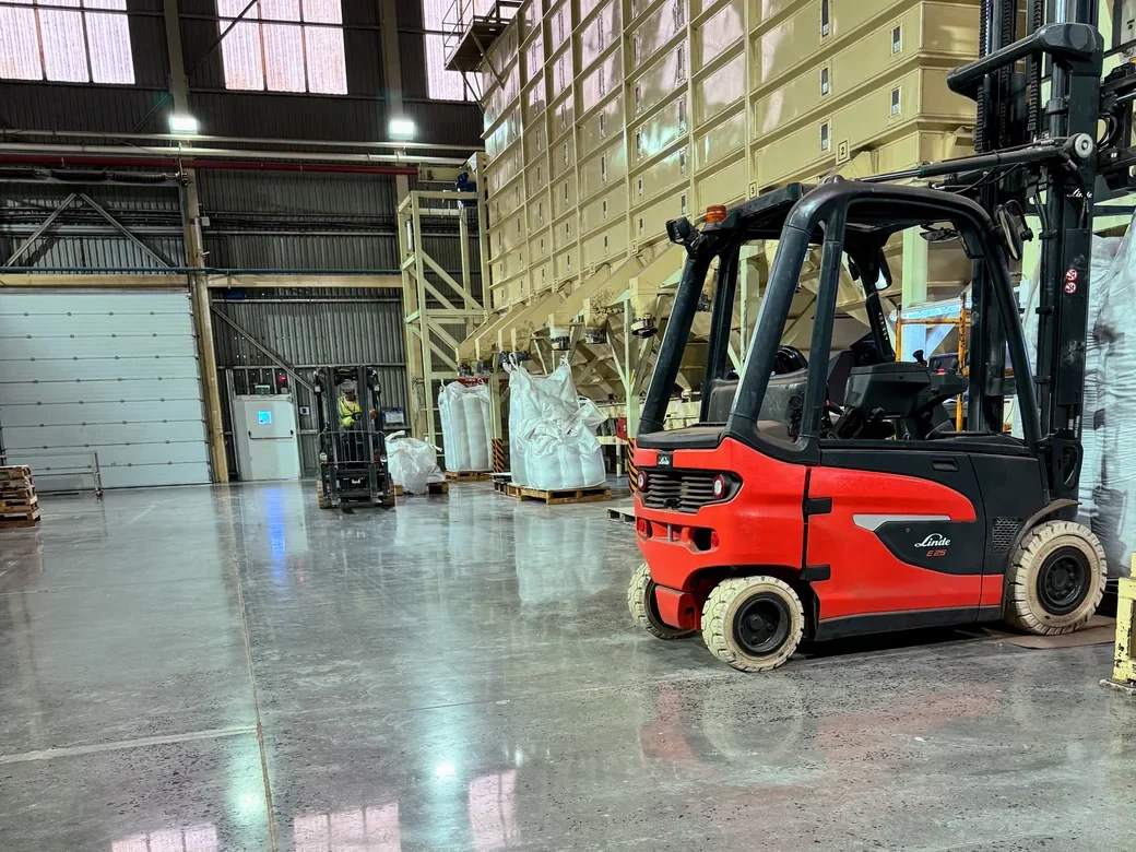 Autoelevador sobre un piso de hormigón pulido en una planta industrial, con la estructura reflejada en la superficie