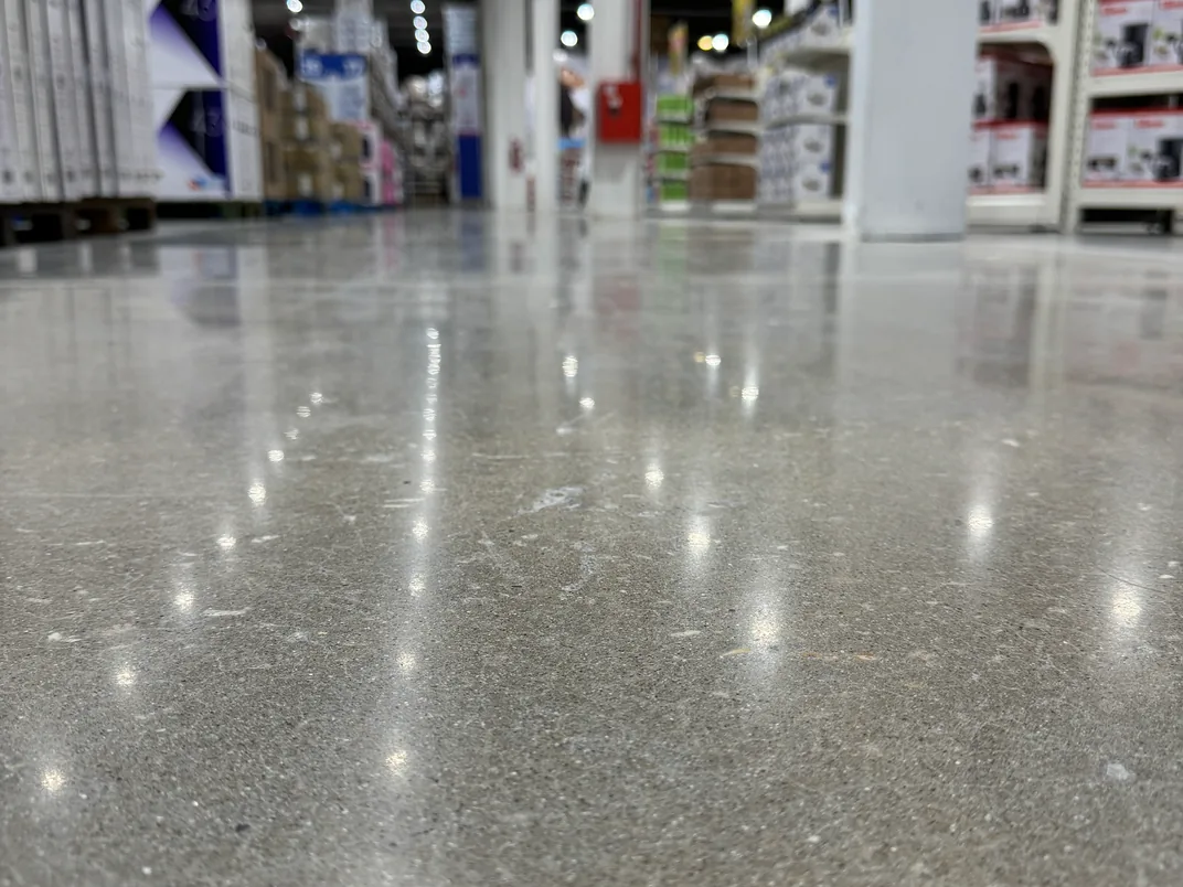 Detalle del piso de hormigón pulido de un supermercado, con el árido a la vista y las luminarias reflejadas