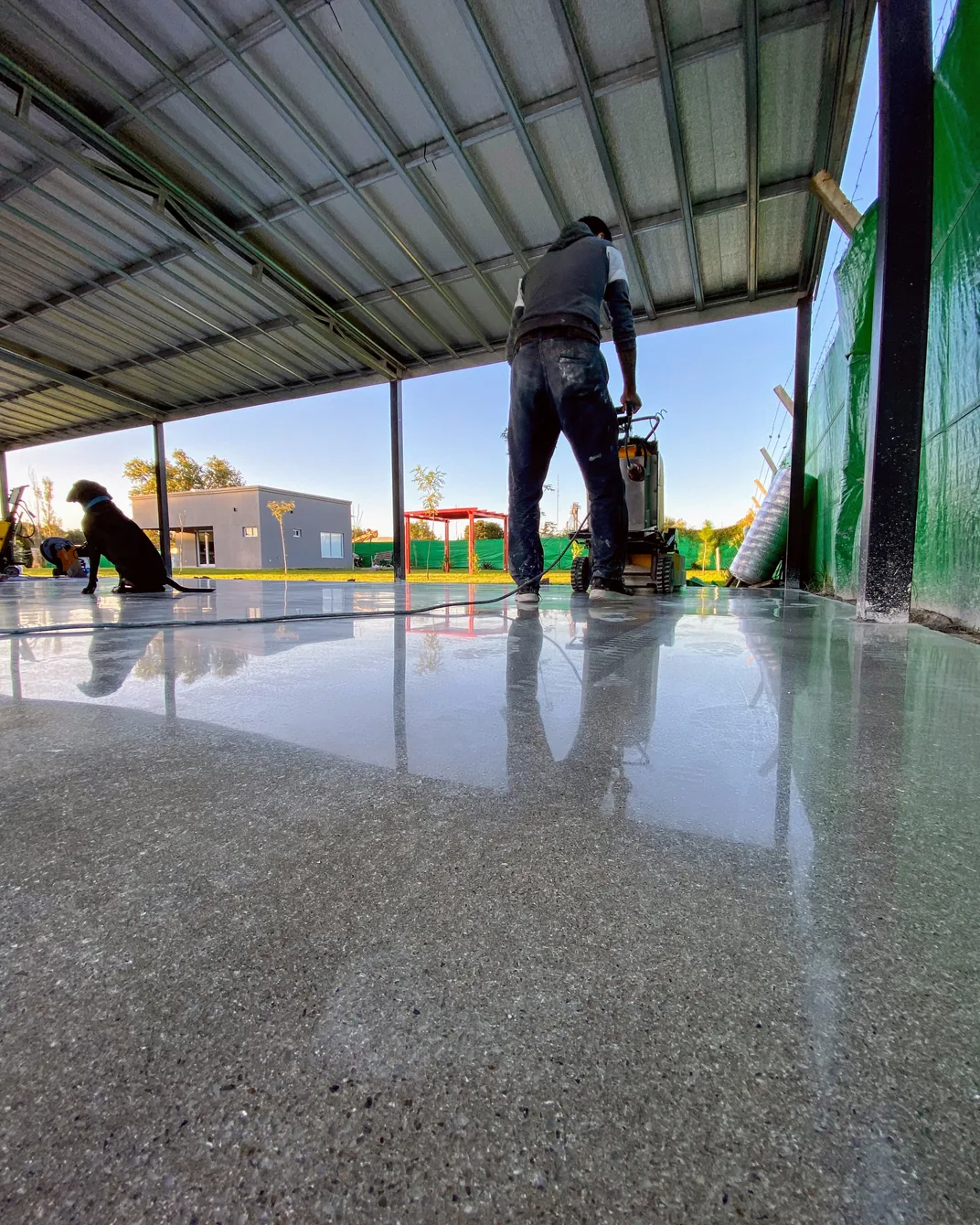 Galería de una vivienda con el piso de hormigón pulido terminado, reflejando el parque y la estructura